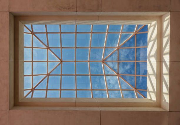 Skylight with a grid of wooden beams against a bright blue sky with clouds.
