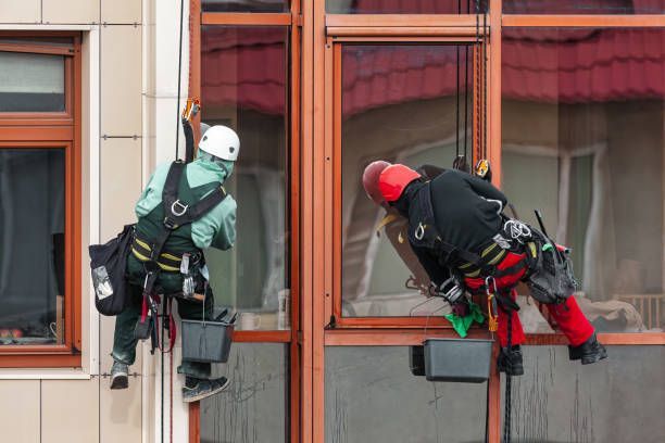Two window cleaners suspended by ropes, cleaning windows on a tall building.