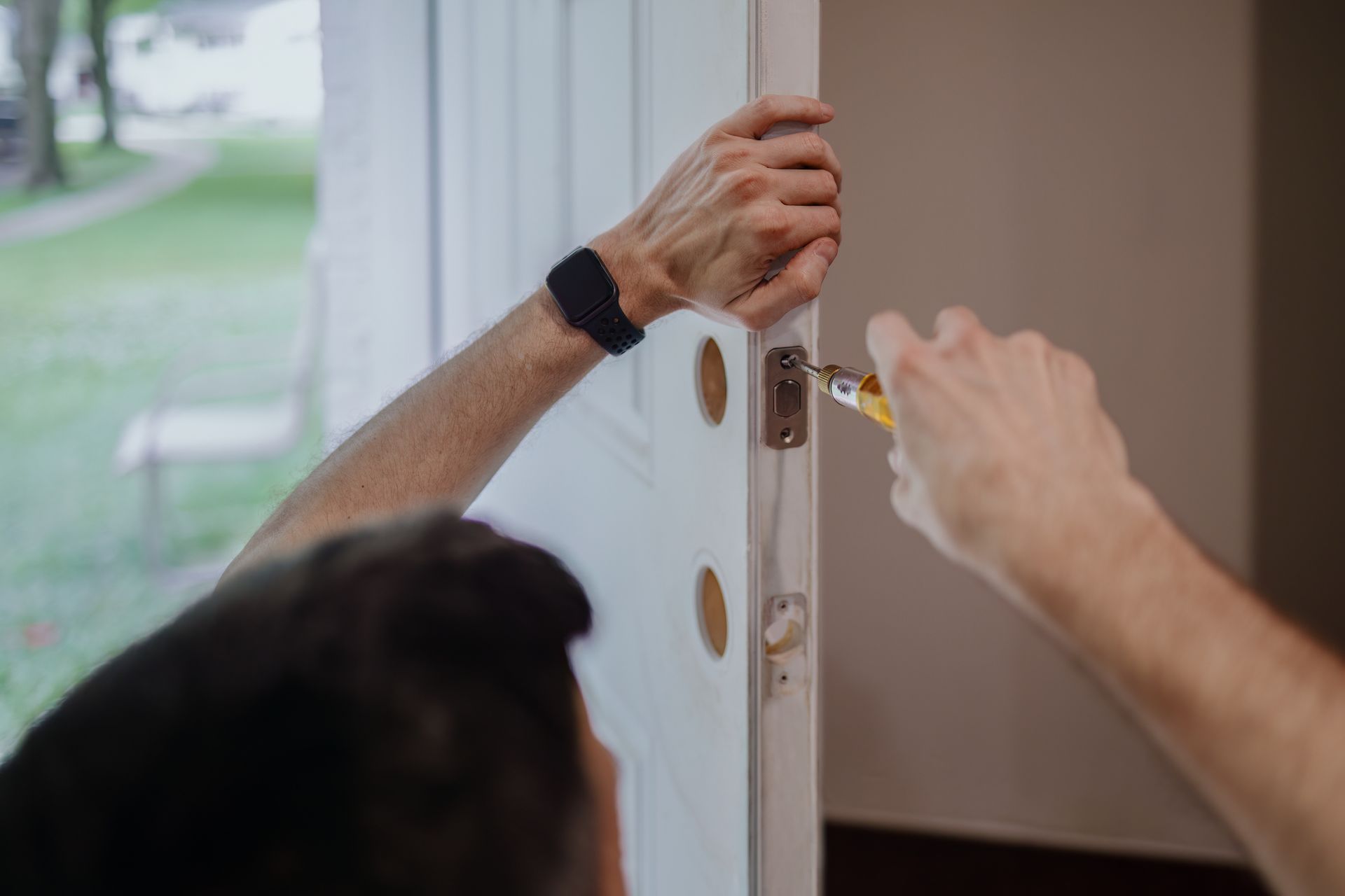 Person using a screwdriver to install a door lock on a white door.