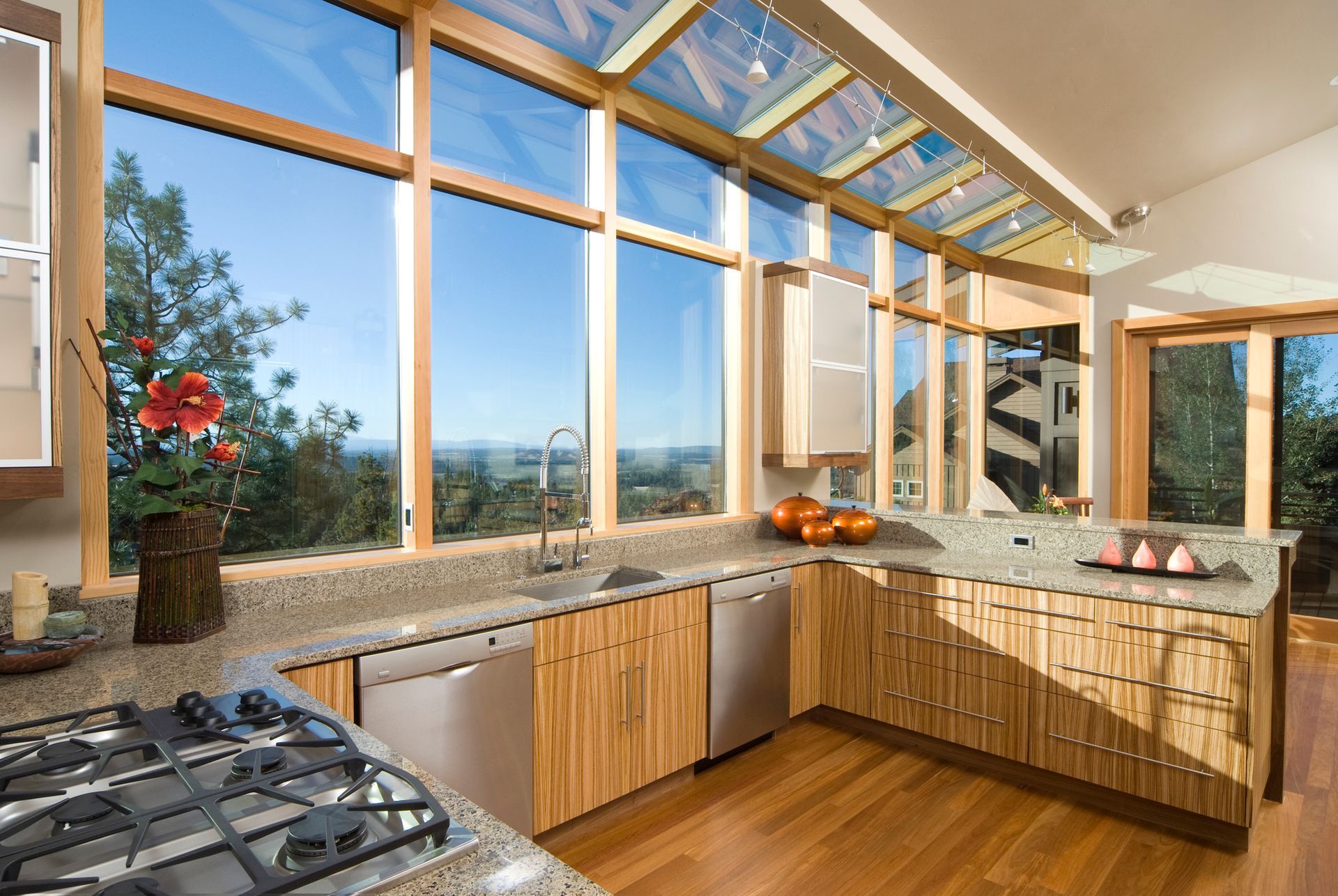 Kitchen with large windows, skylights, wood cabinets, granite countertops, stainless steel appliances, and a view of trees and sky.