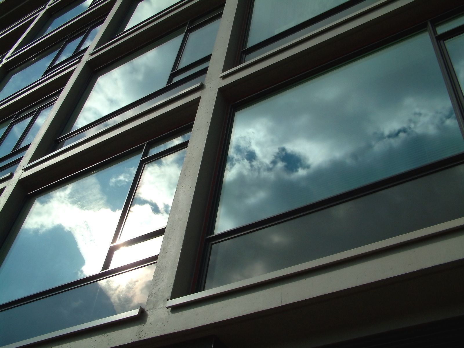 Building facade with many windows reflecting a cloudy sky.