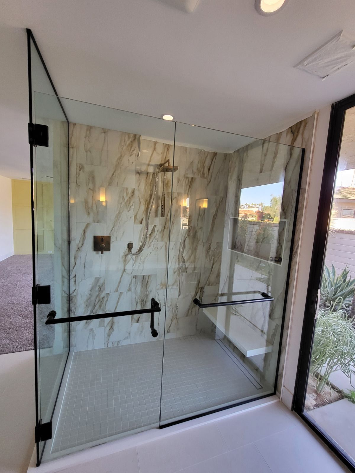 Modern glass shower with black fixtures and marble-look tile.