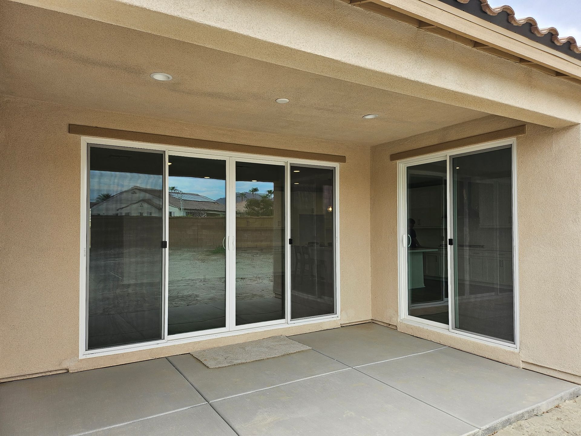 Covered patio with sliding glass doors, tan stucco walls, and concrete floor.