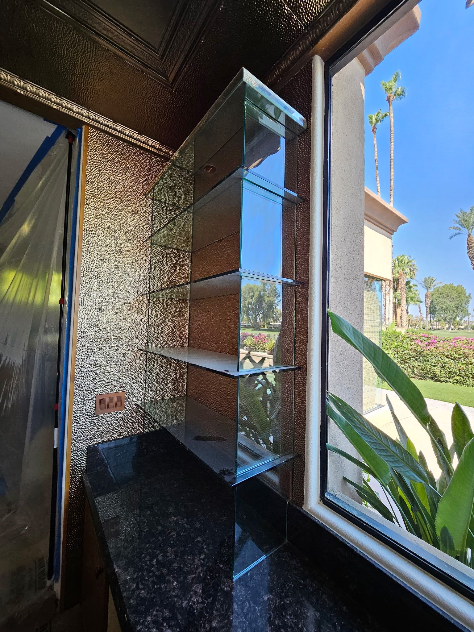 Glass shelves against a sparkling mosaic wall next to a window with an outdoor view.