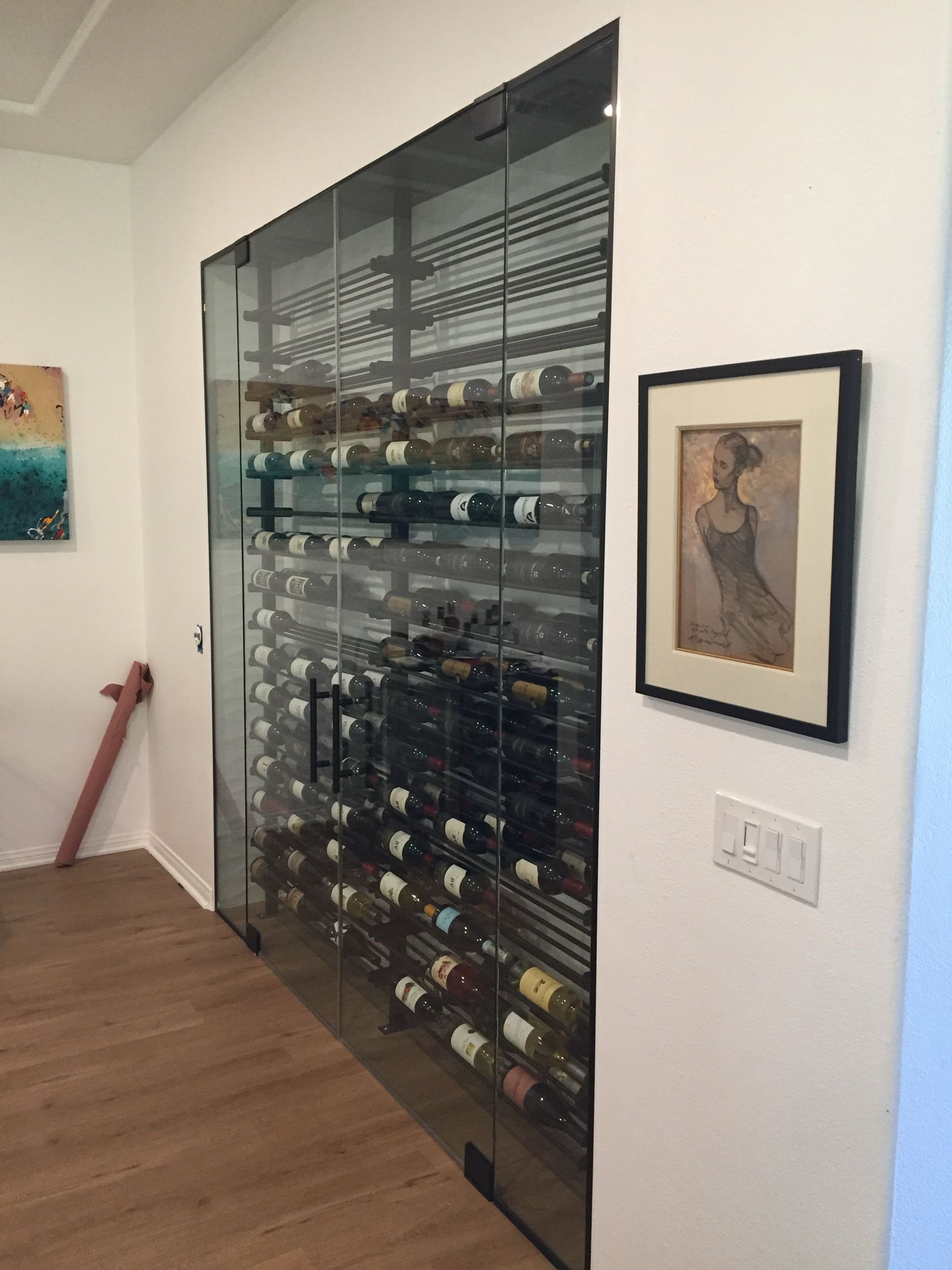 Wine cellar with glass door, showcasing numerous wine bottles on racks, built into a white wall.