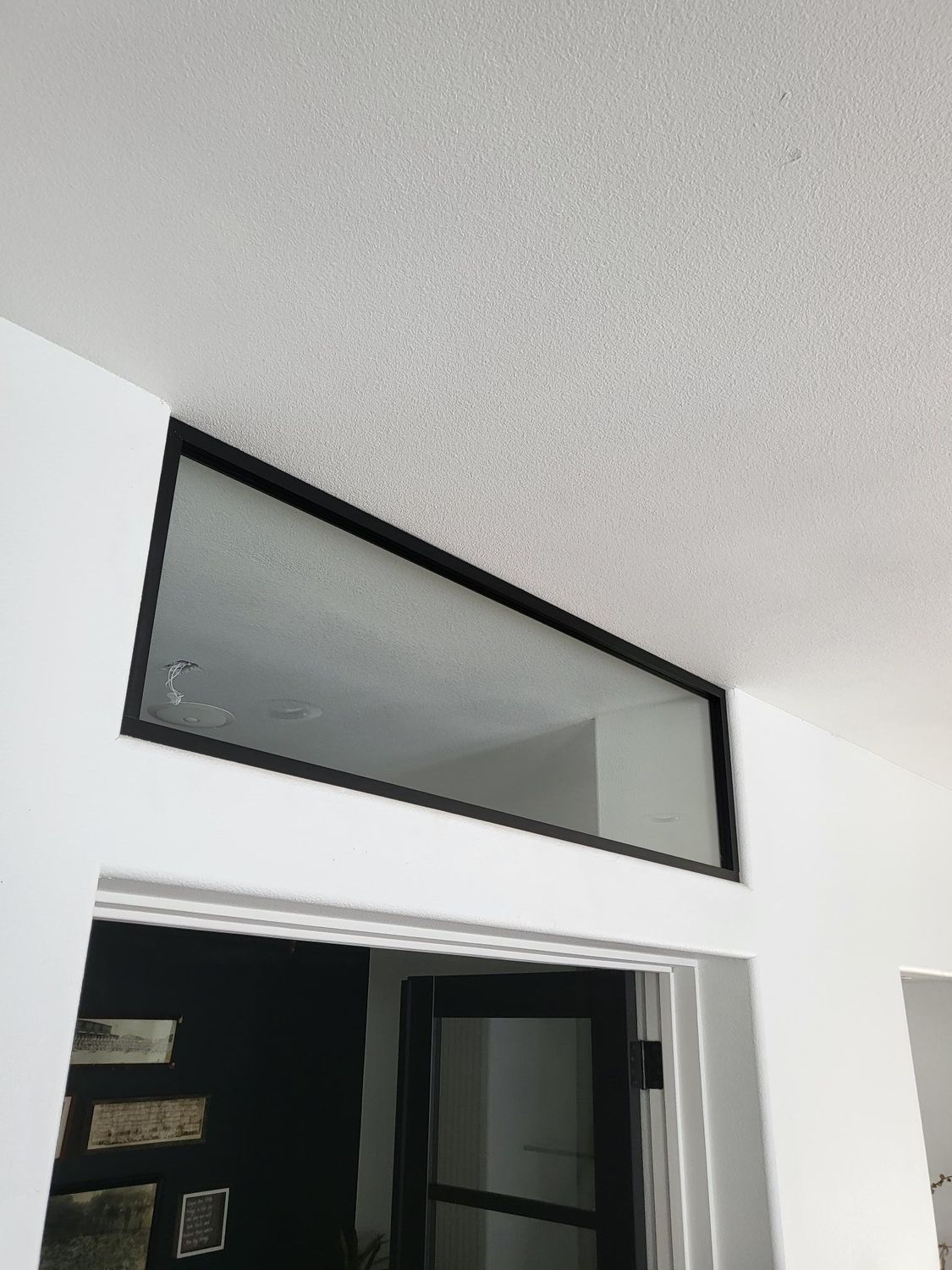 Black-framed rectangular window above an interior door. White walls and textured ceiling are visible.