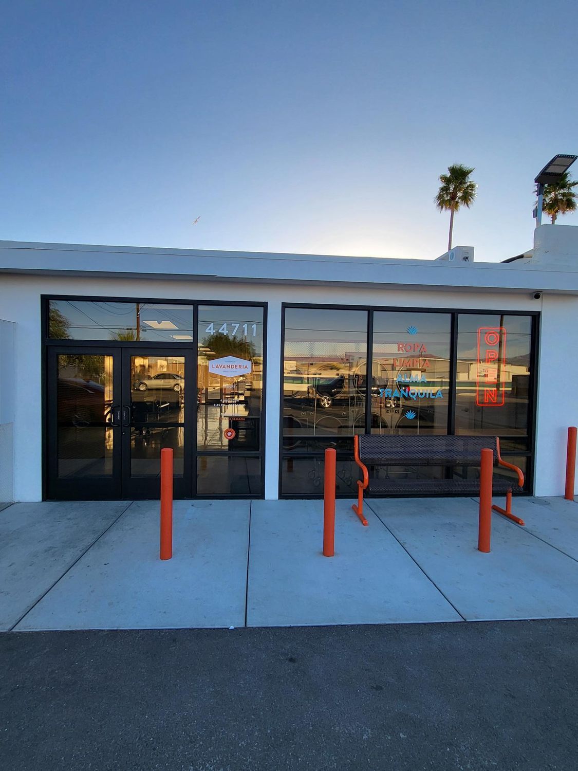Exterior of a building with large windows. The building is white with black trim. An orange bench sits outside.