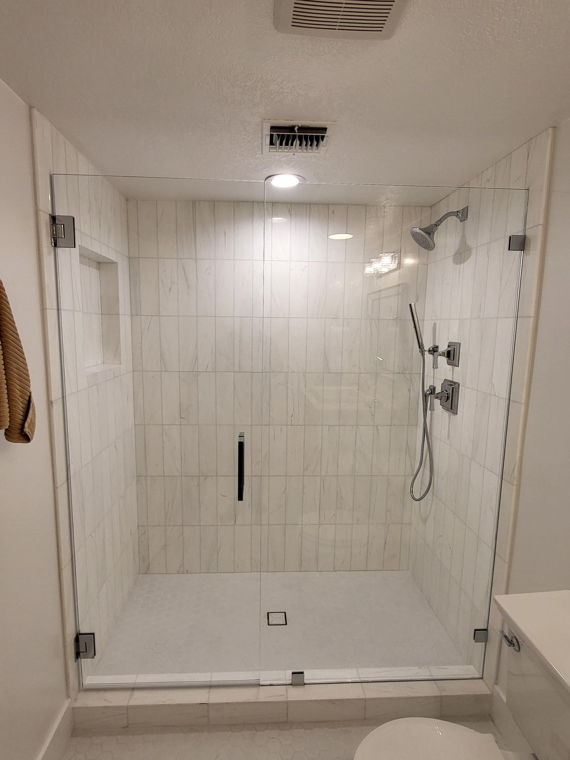 Glass-enclosed shower with white tiled walls, chrome fixtures, and a glass door.