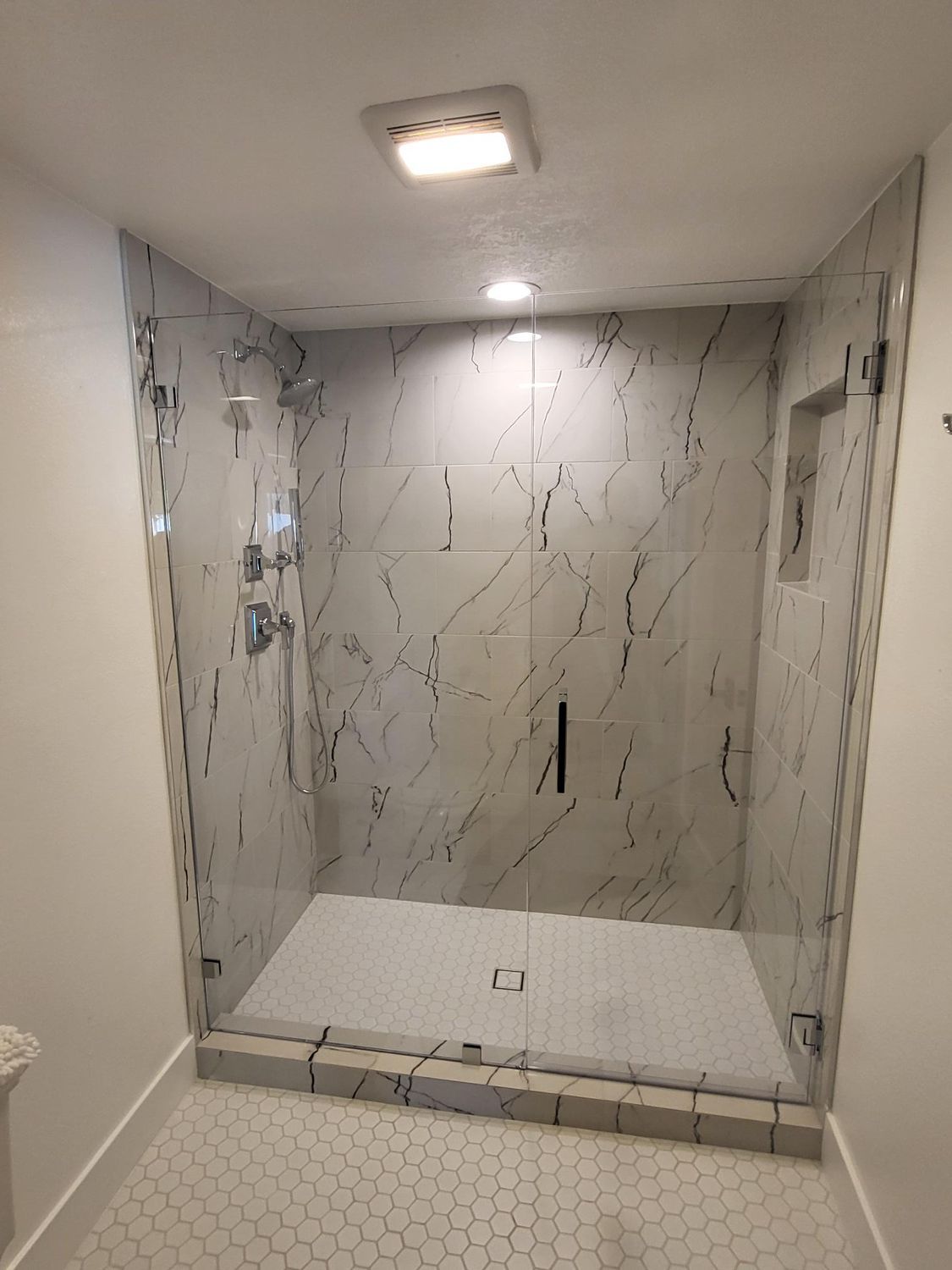 Modern shower with marble-look tile walls, glass doors, and a small recessed shelf.