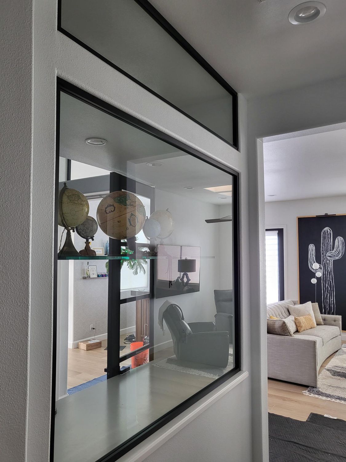 Glass-enclosed display case with black trim built into a wall, showcasing globes and items. Interior room visible beyond.