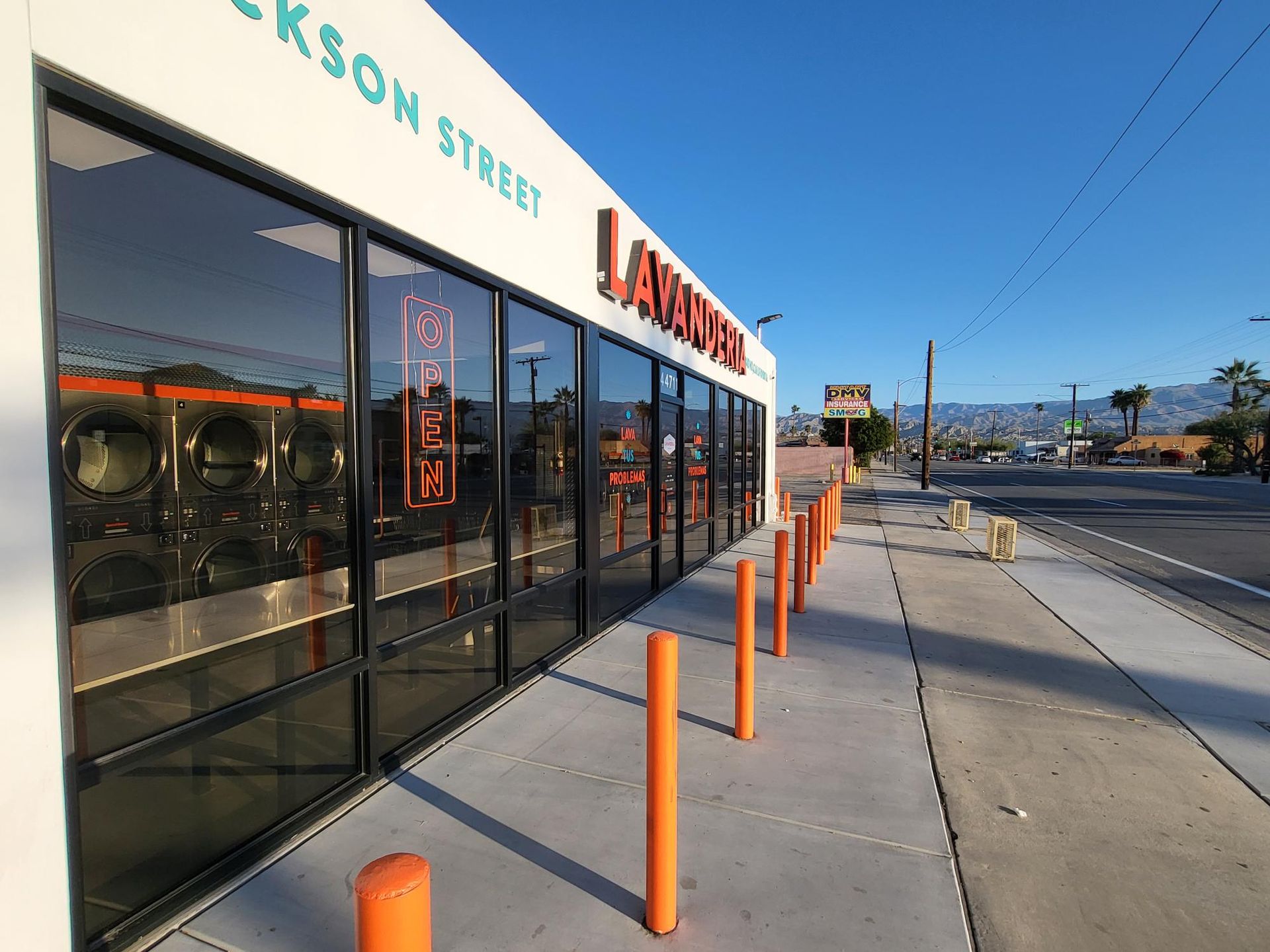 Exterior of a laundromat on Jackson Street with orange bollards, glass windows, and a clear blue sky.