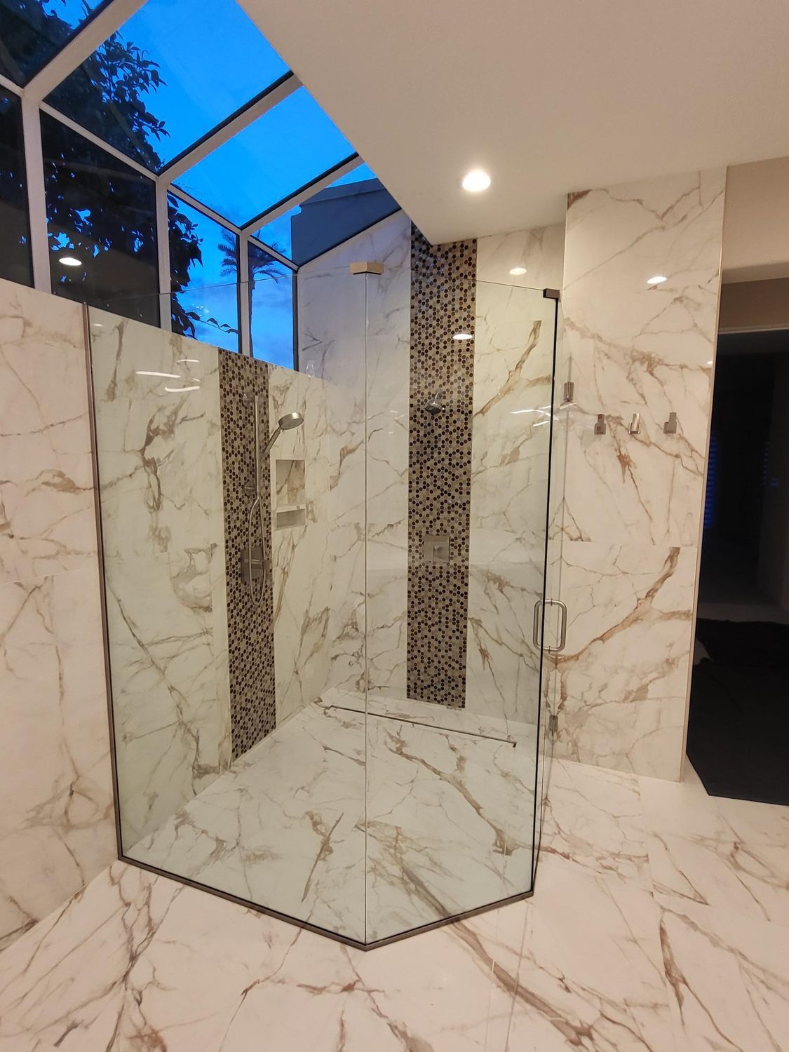 Modern shower with white marble walls and a glass enclosure under a skylight.