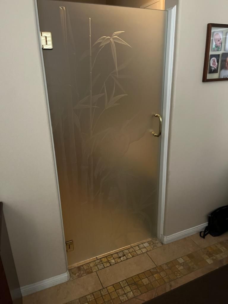 Glass shower door with etched bamboo design, brass hardware, and tiled floor.
