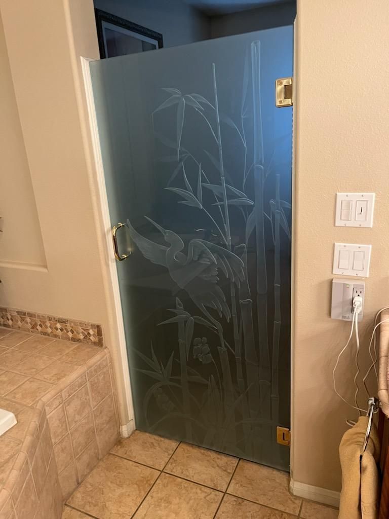 Shower door with etched bamboo and heron design. Gold hardware and tile floor.