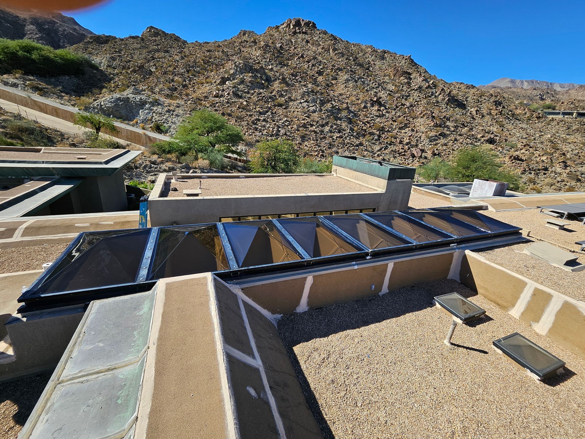 Rooftop with solar panels and gravel; rocky mountain backdrop, sunny day.