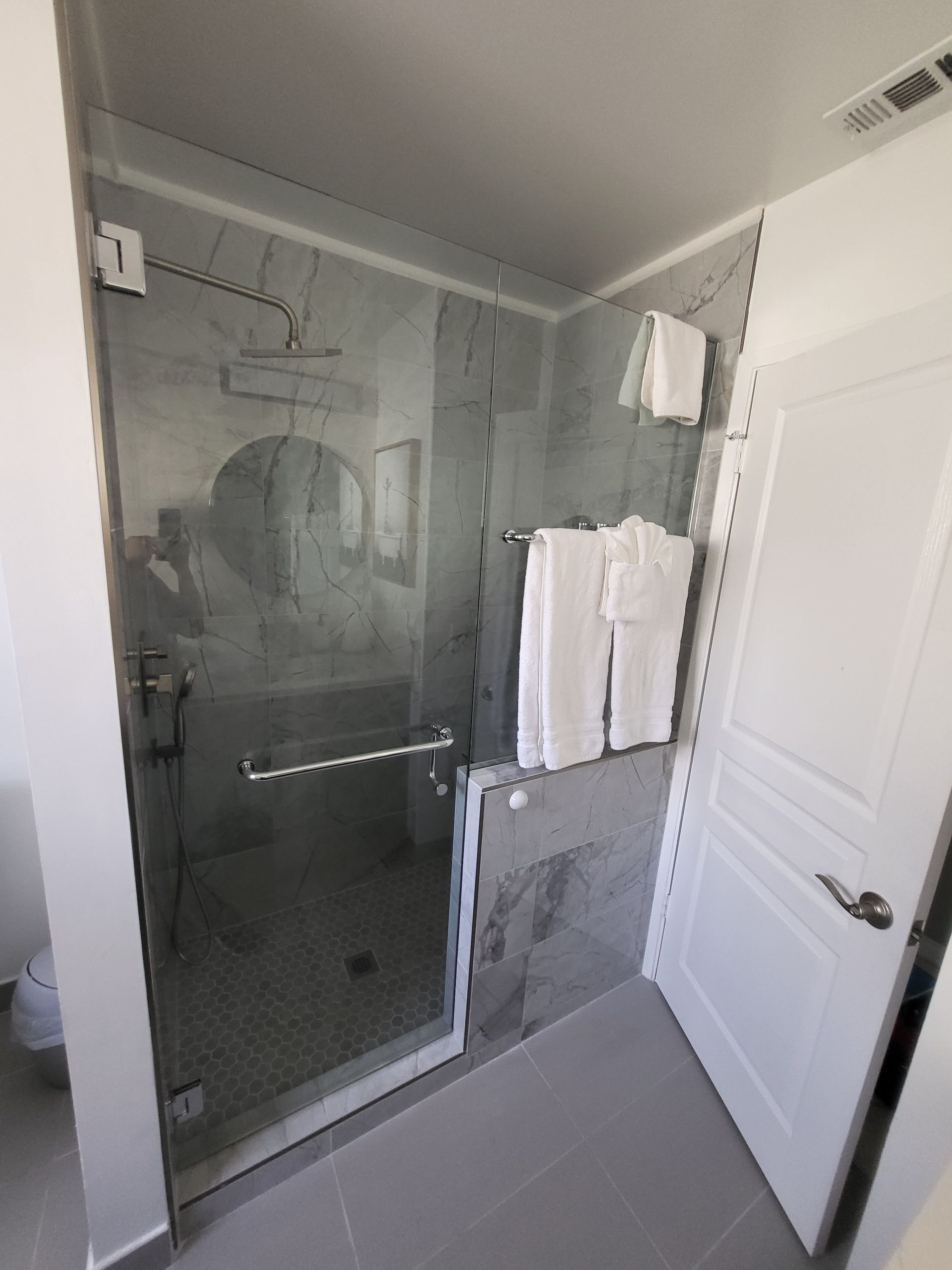 Shower with glass door, gray tile, white towels, and a white door.