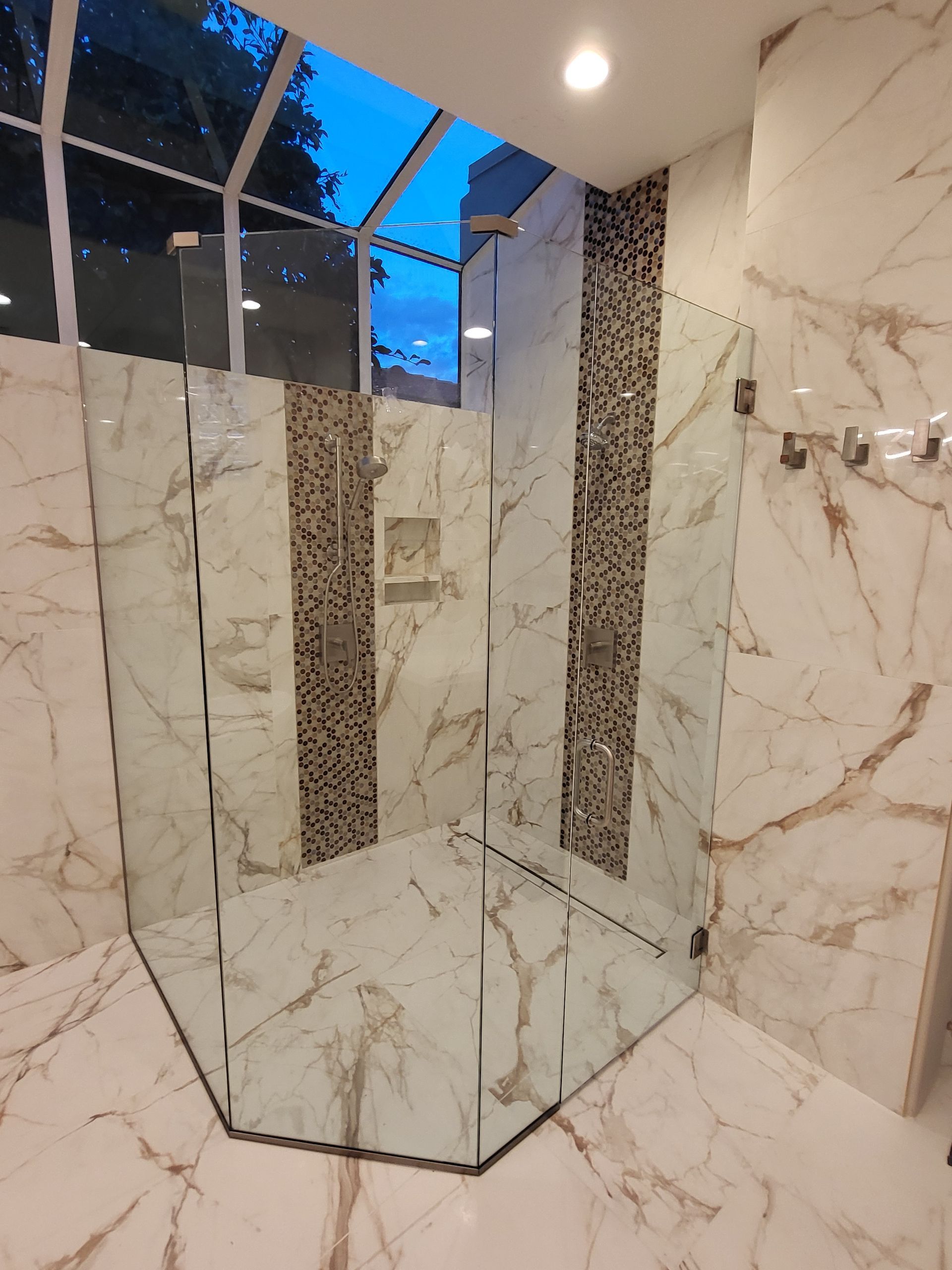 Glass shower enclosure with marble and mosaic tile.