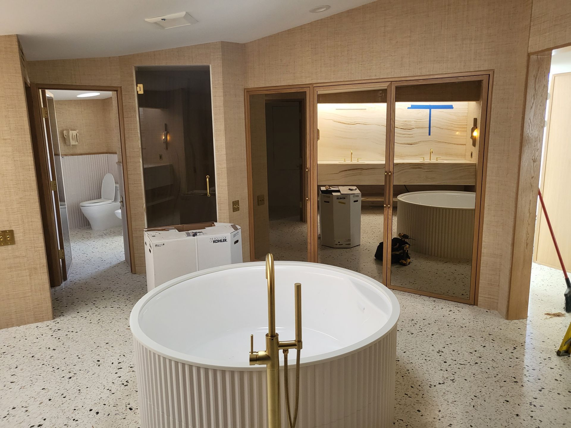 Luxurious bathroom with a circular tub, gold faucet, and textured walls; view of toilet and sinks.