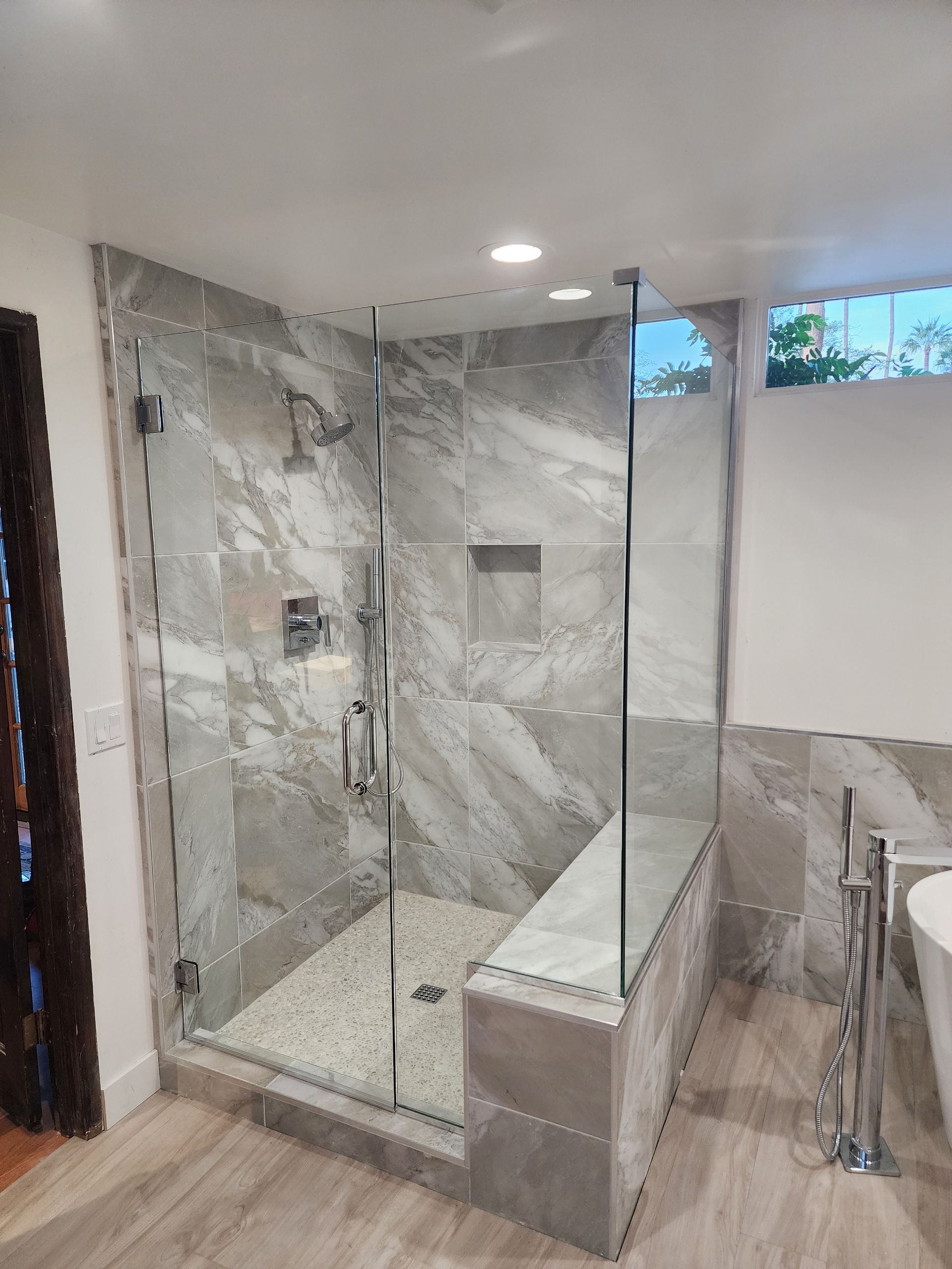 Modern bathroom with glass shower enclosure, gray marble tile, and a bench seat.