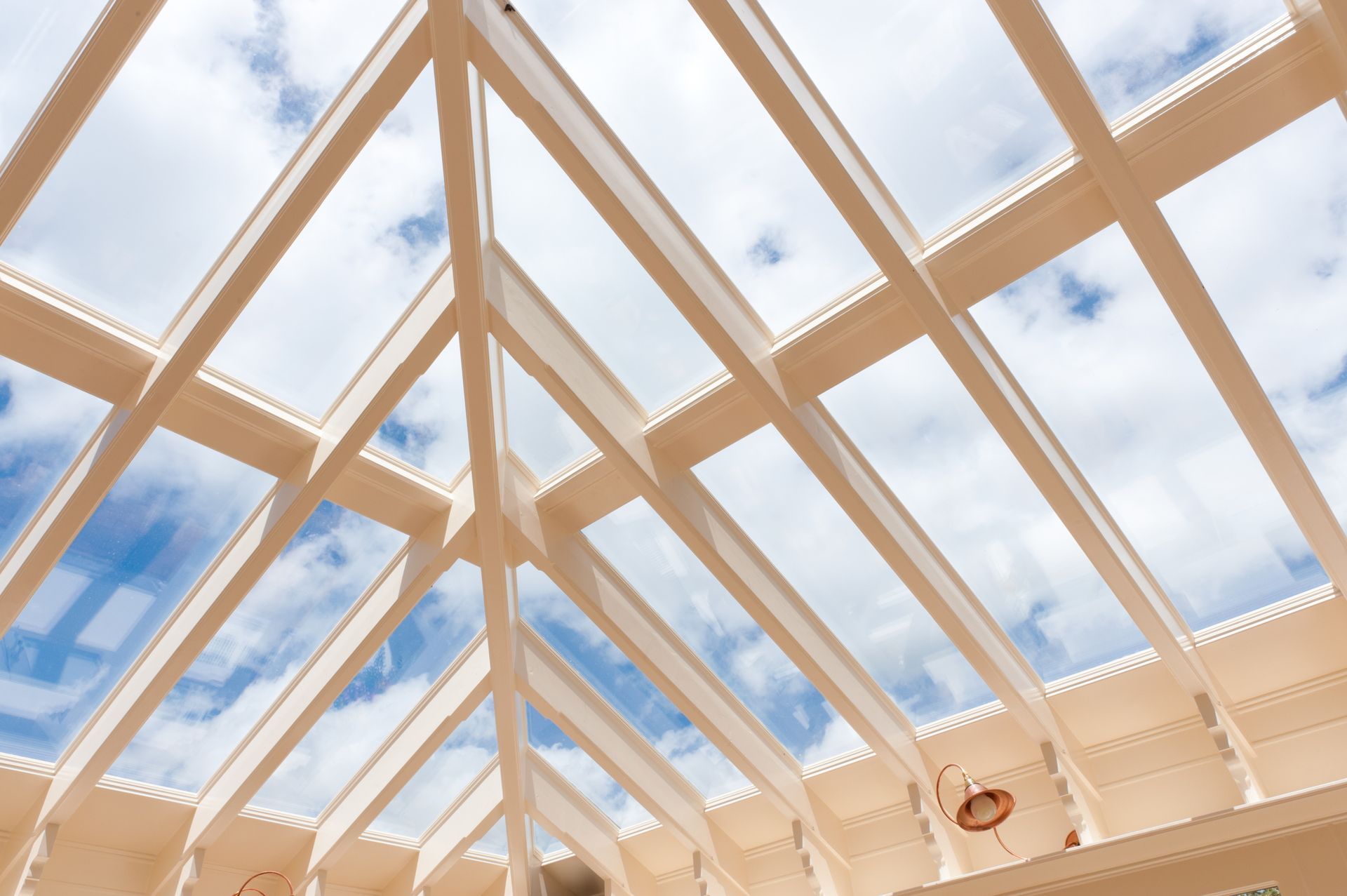 White, geometric skylight with glass panes against a blue sky with clouds.