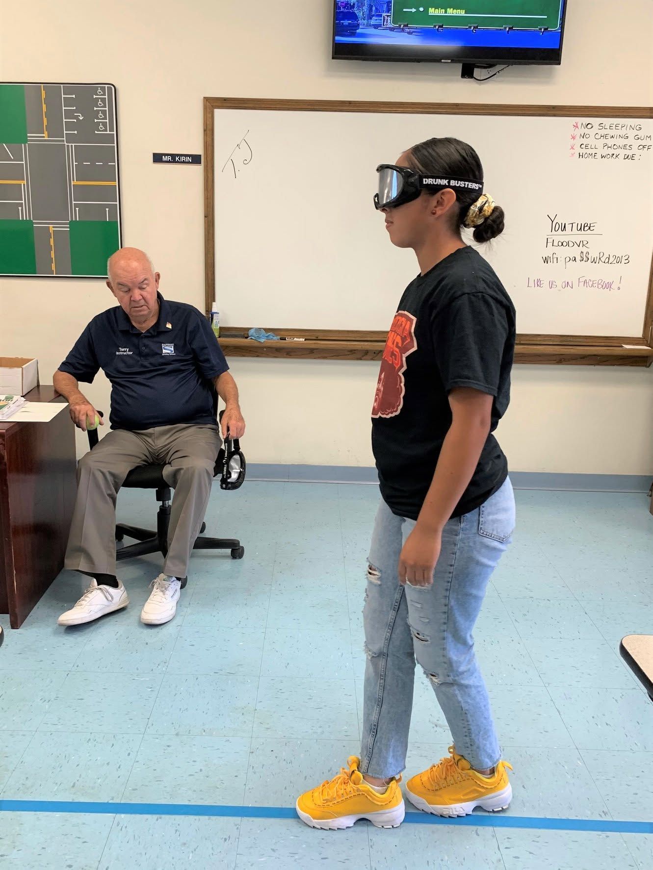 Person wearing a VR headset in a classroom while another person sits nearby.