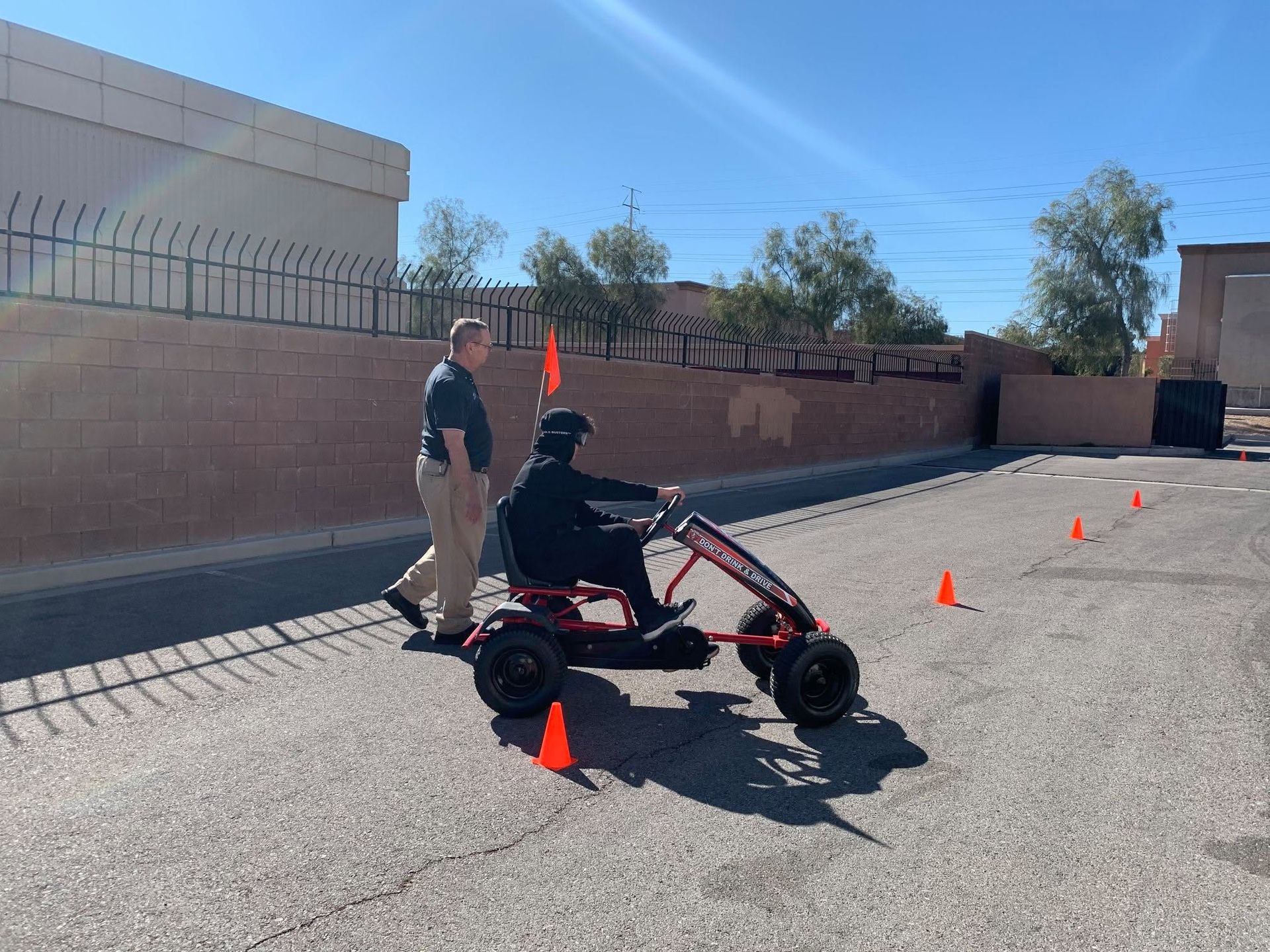 Person driving a red mobility scooter through an outdoor cone course while another stands nearby