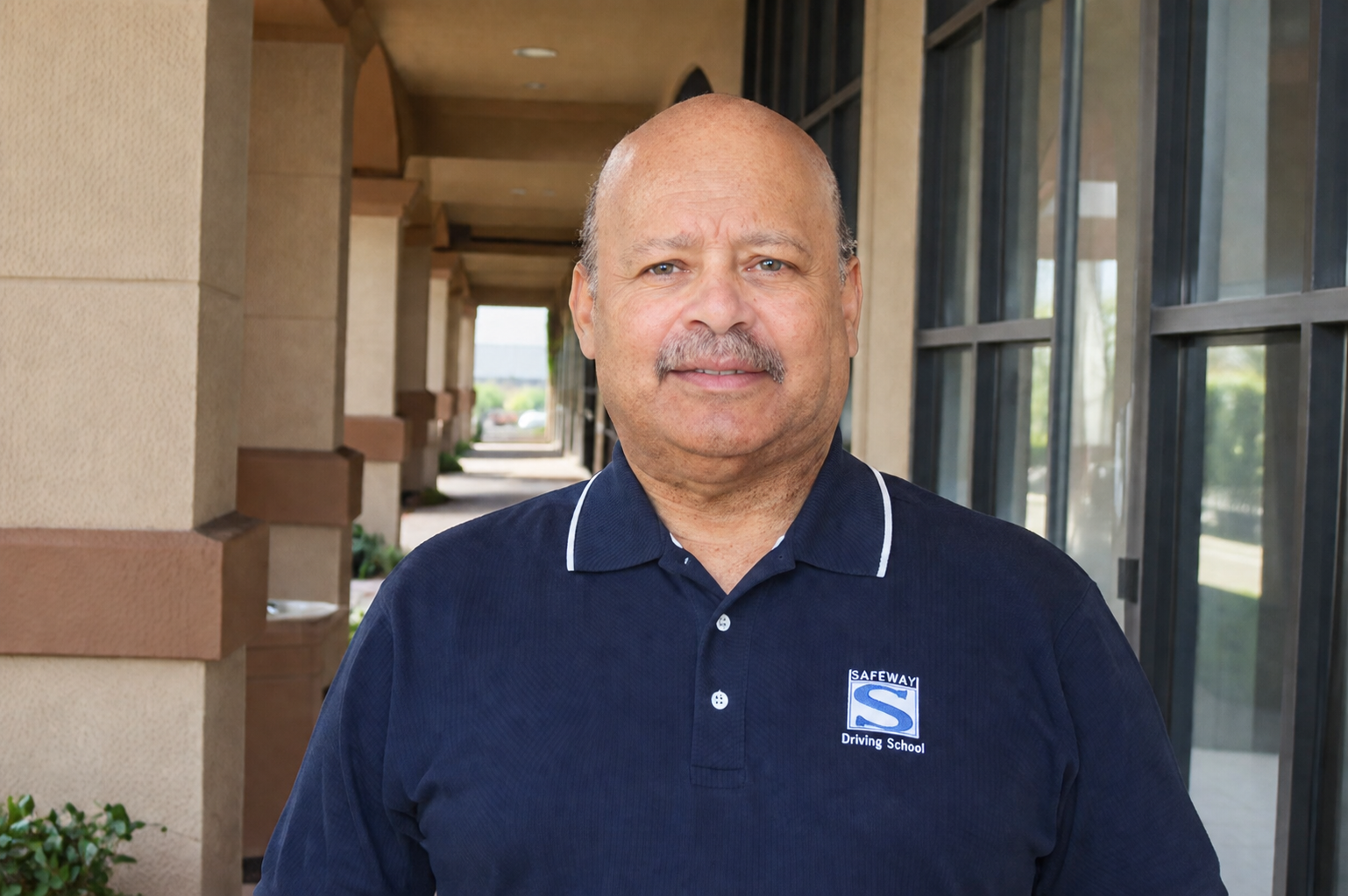 Man in navy polo shirt standing in a sunlit outdoor corridor next to building columns