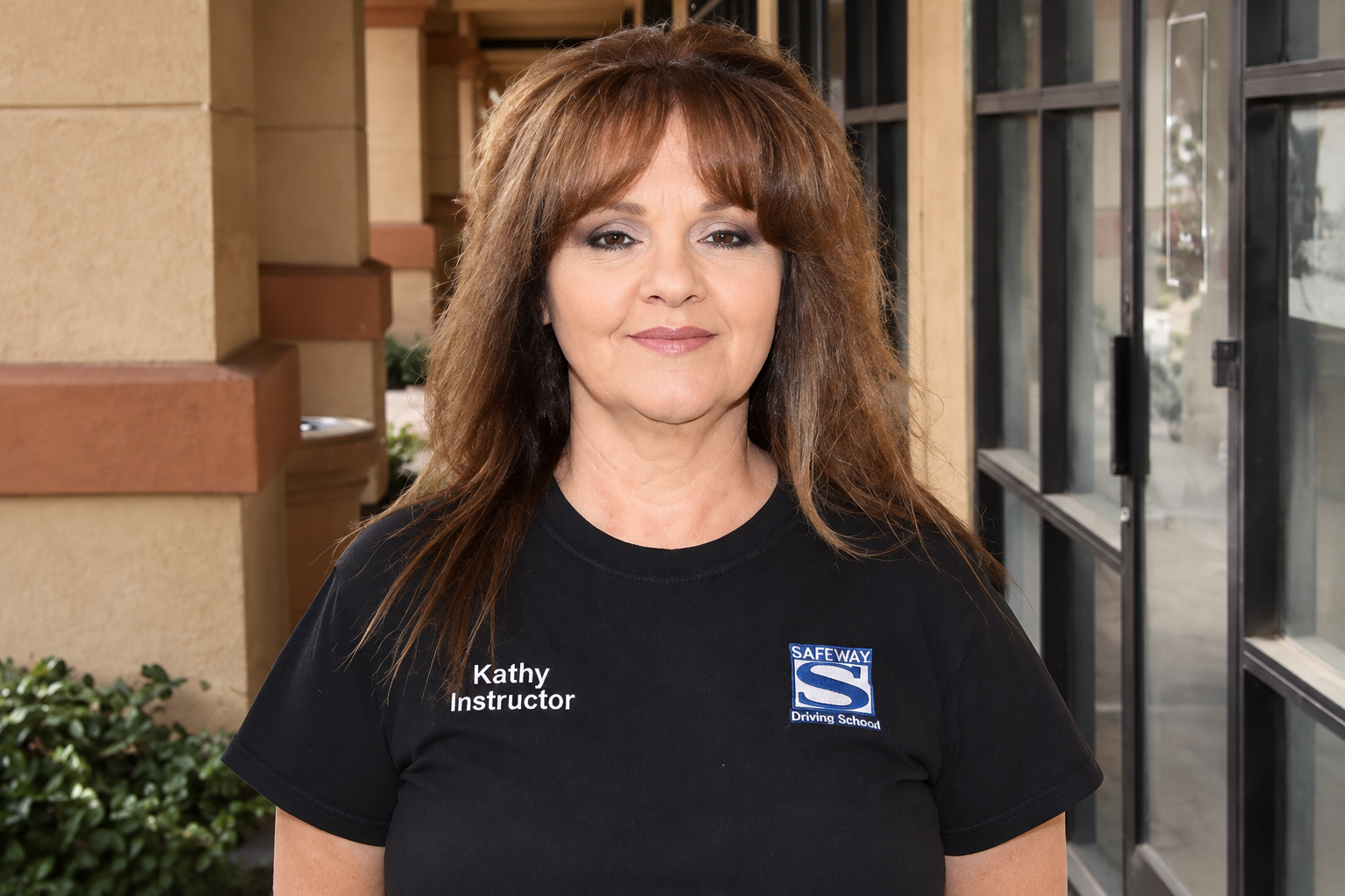 Woman in black T-shirt standing outdoors by a building entrance, smiling at the camera.