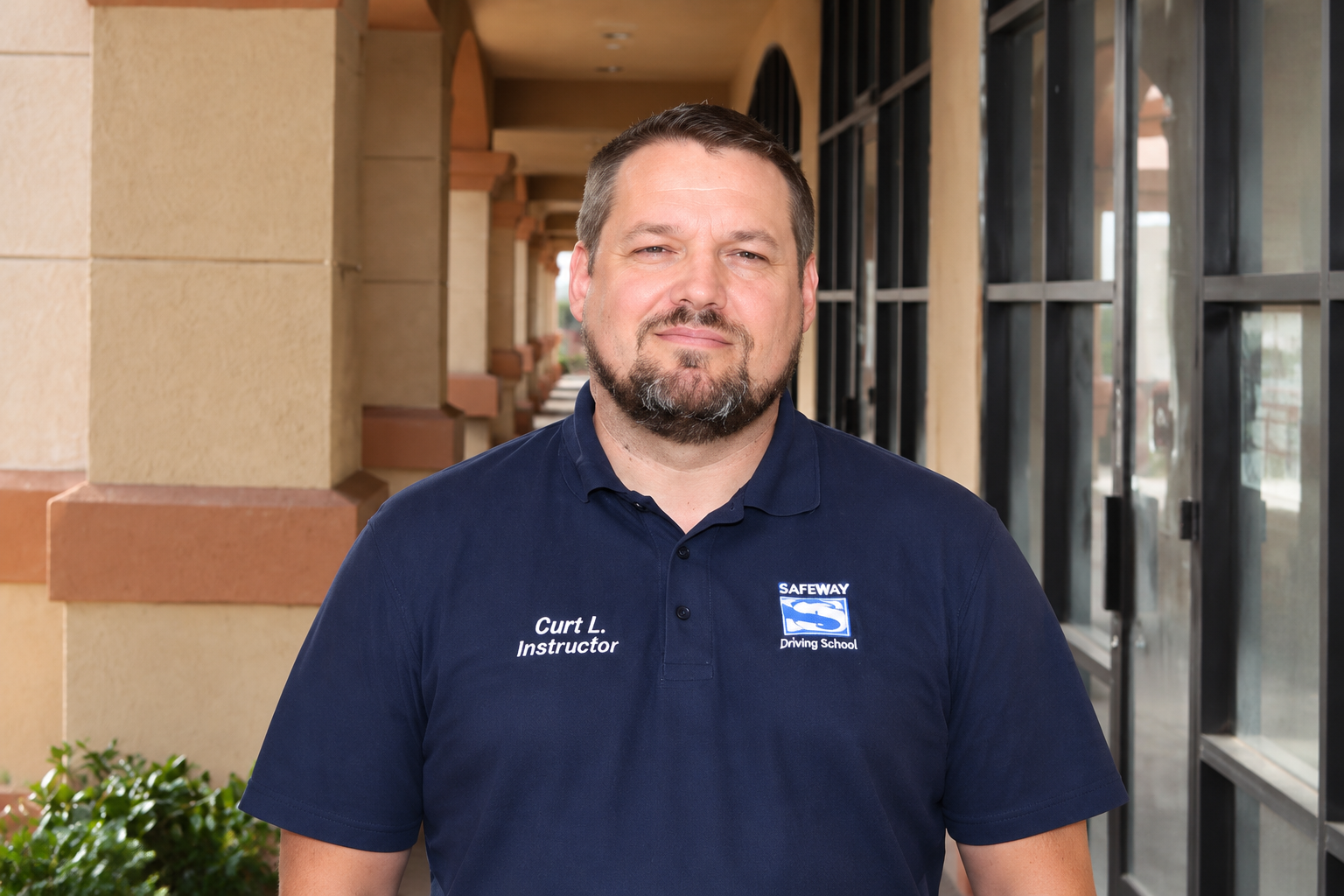 Man in a navy polo shirt standing outdoors by a building entrance