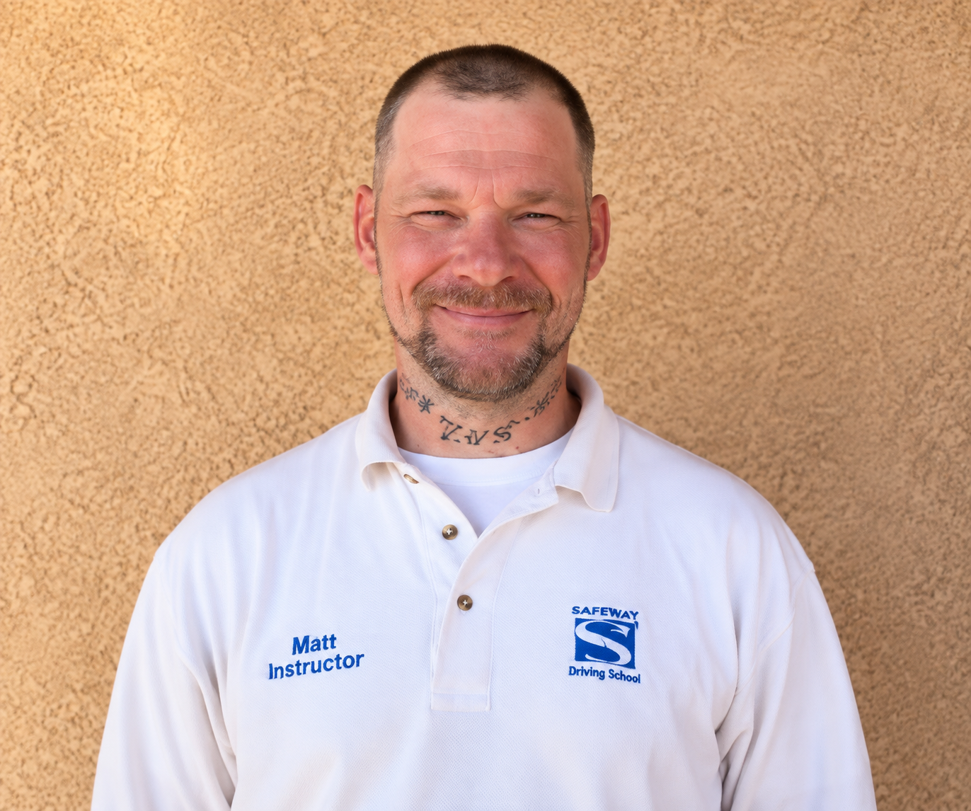 Smiling man in white collared shirt standing against a tan stucco wall