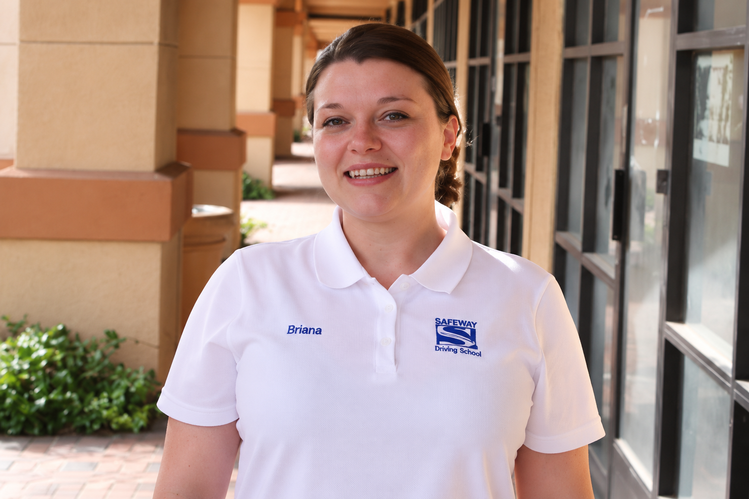 Person in a white polo shirt standing outside a building, smiling at the camera.