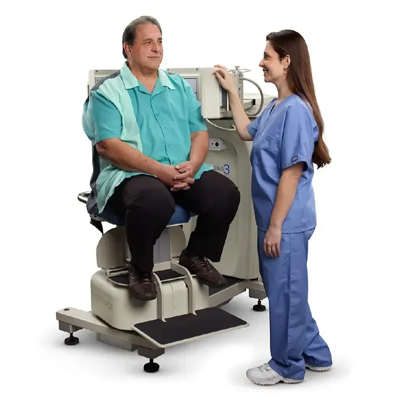 Man seated in medical chair, being assisted by a healthcare worker. Machine is beige and gray; worker wears blue scrubs.