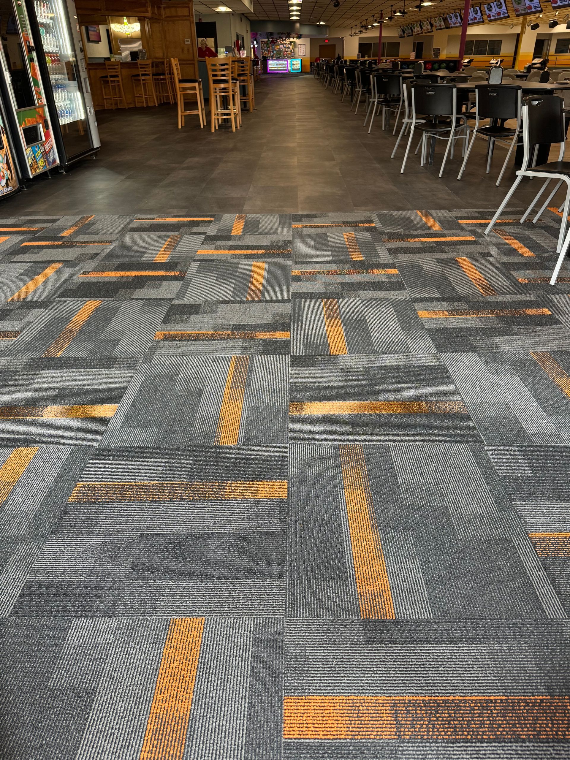 A carpeted floor in a bowling alley with tables and chairs.