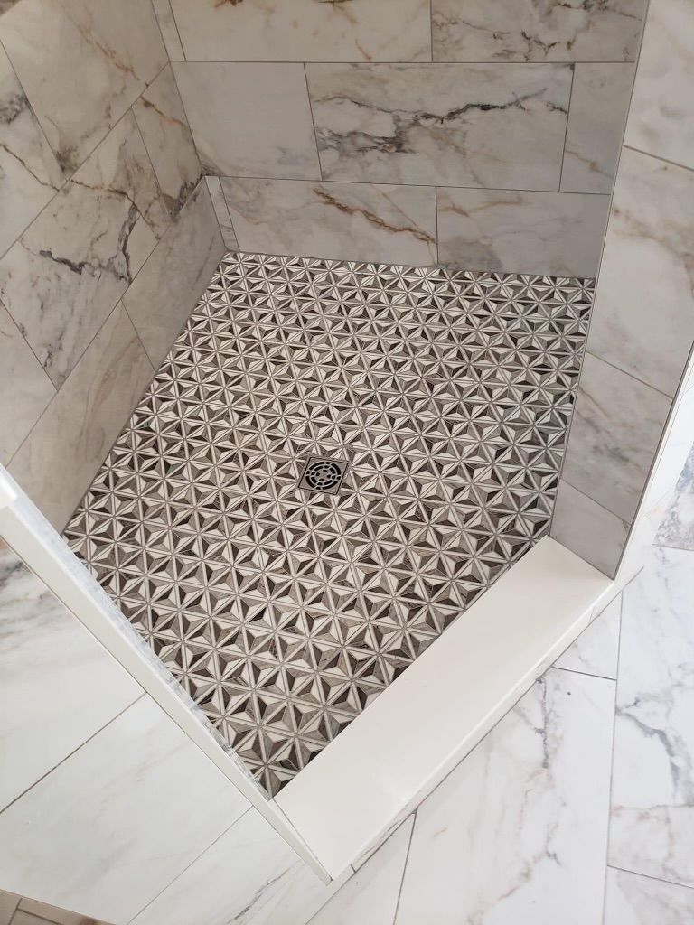 A shower stall with a patterned tile floor and marble walls.