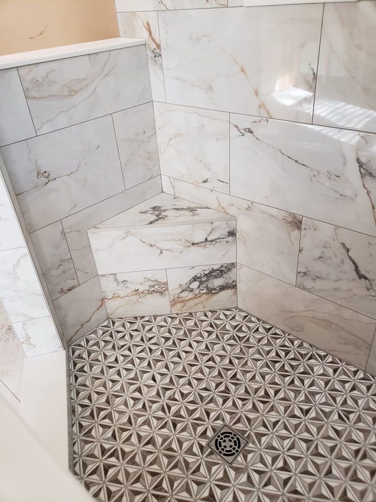 A shower stall with marble tiles and a drain.