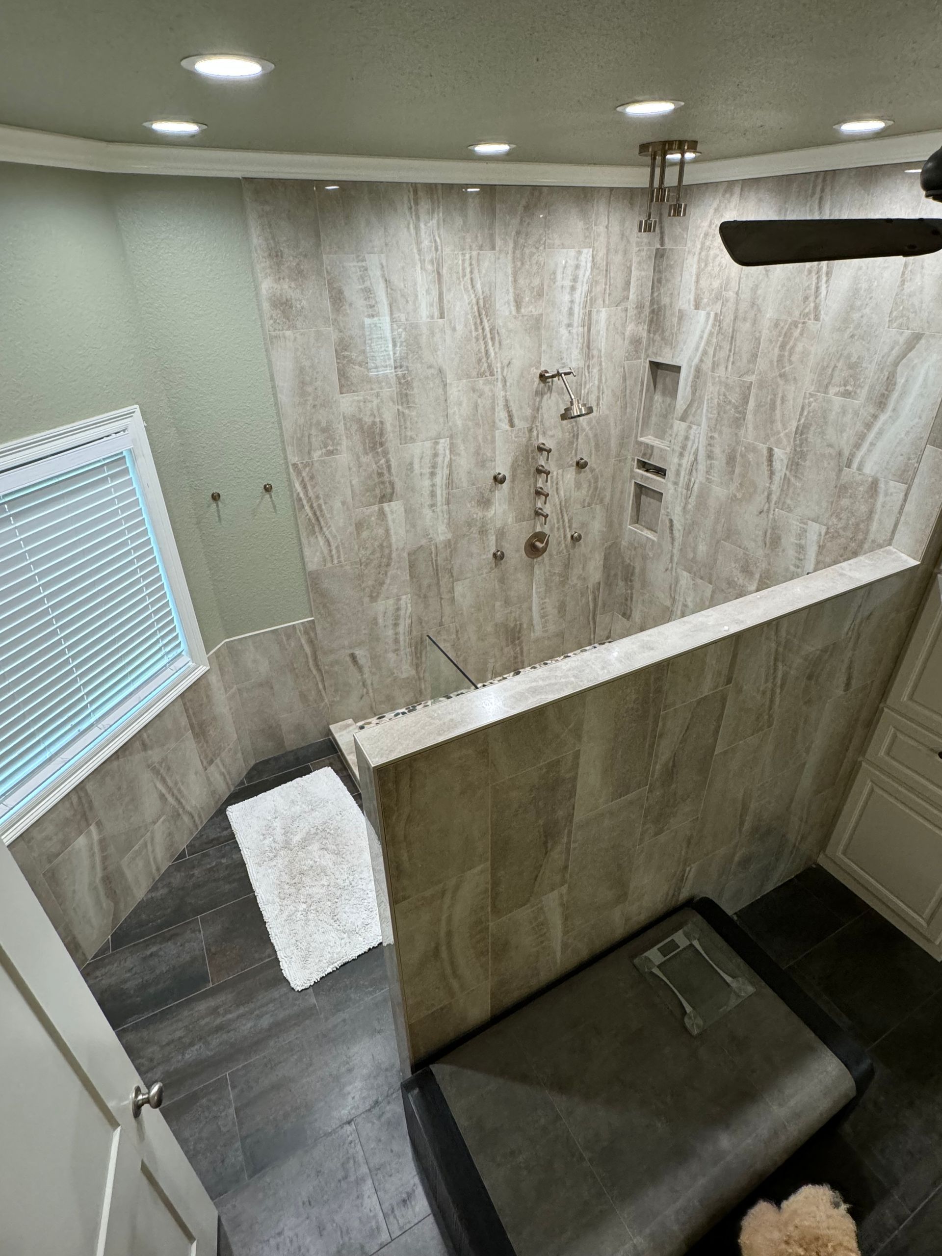 A bathroom with a walk in shower and a ceiling fan.
