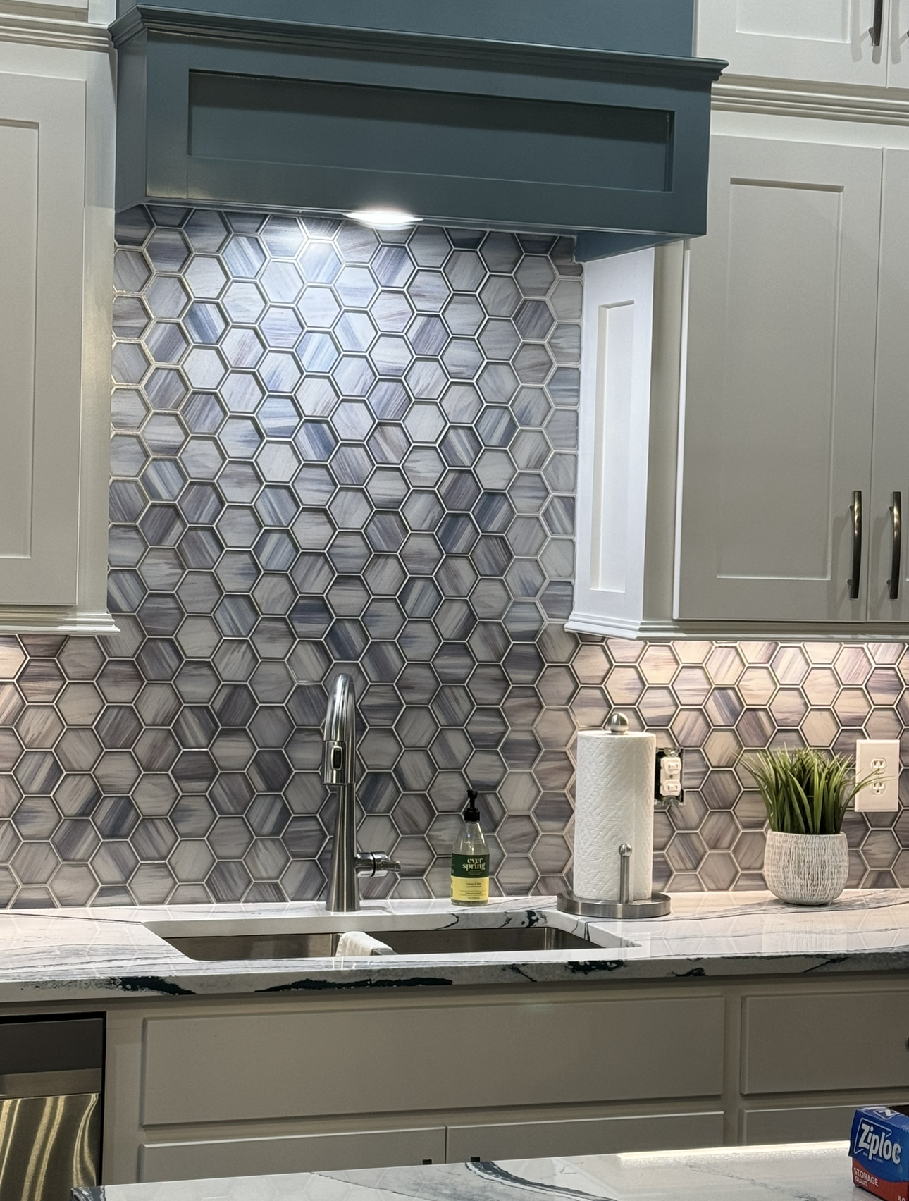 A kitchen with a sink , cabinets , and a hood.
