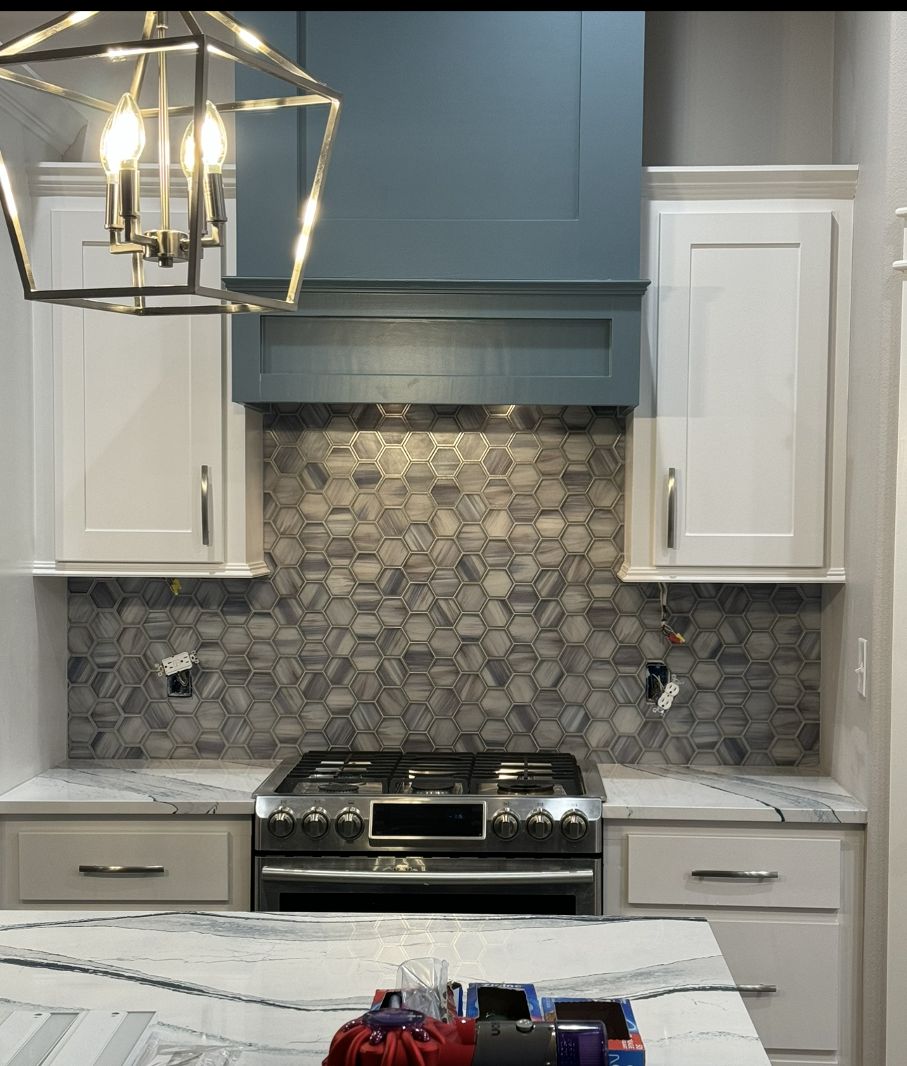 A kitchen with white cabinets , a stove , and a chandelier hanging from the ceiling.