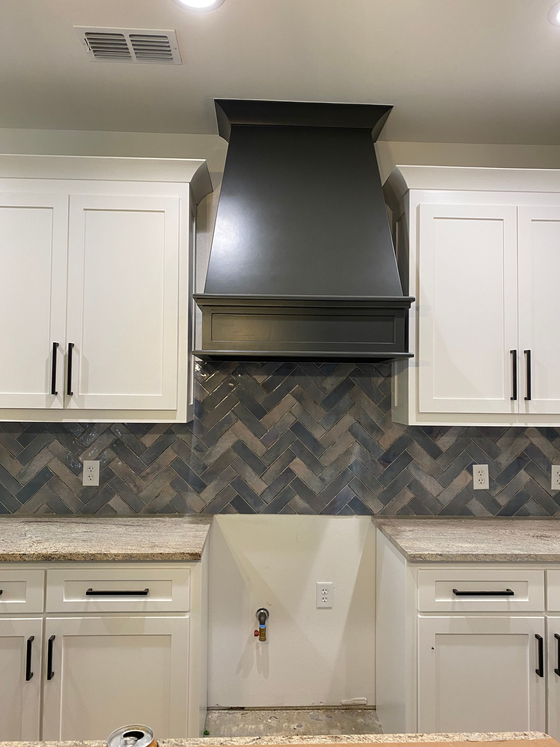 A kitchen with white cabinets and a black hood