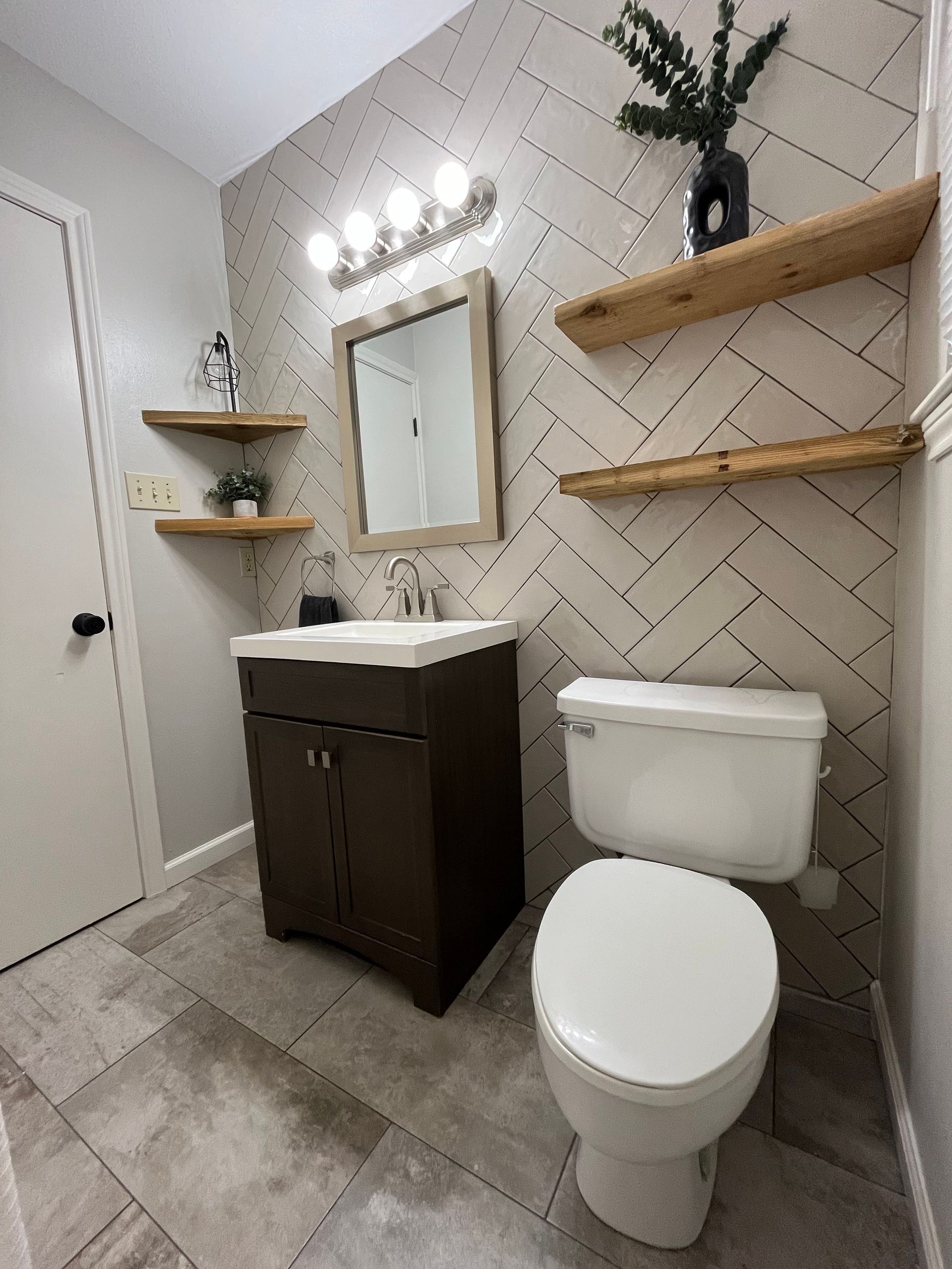 A bathroom with a toilet , sink , mirror and shelves.