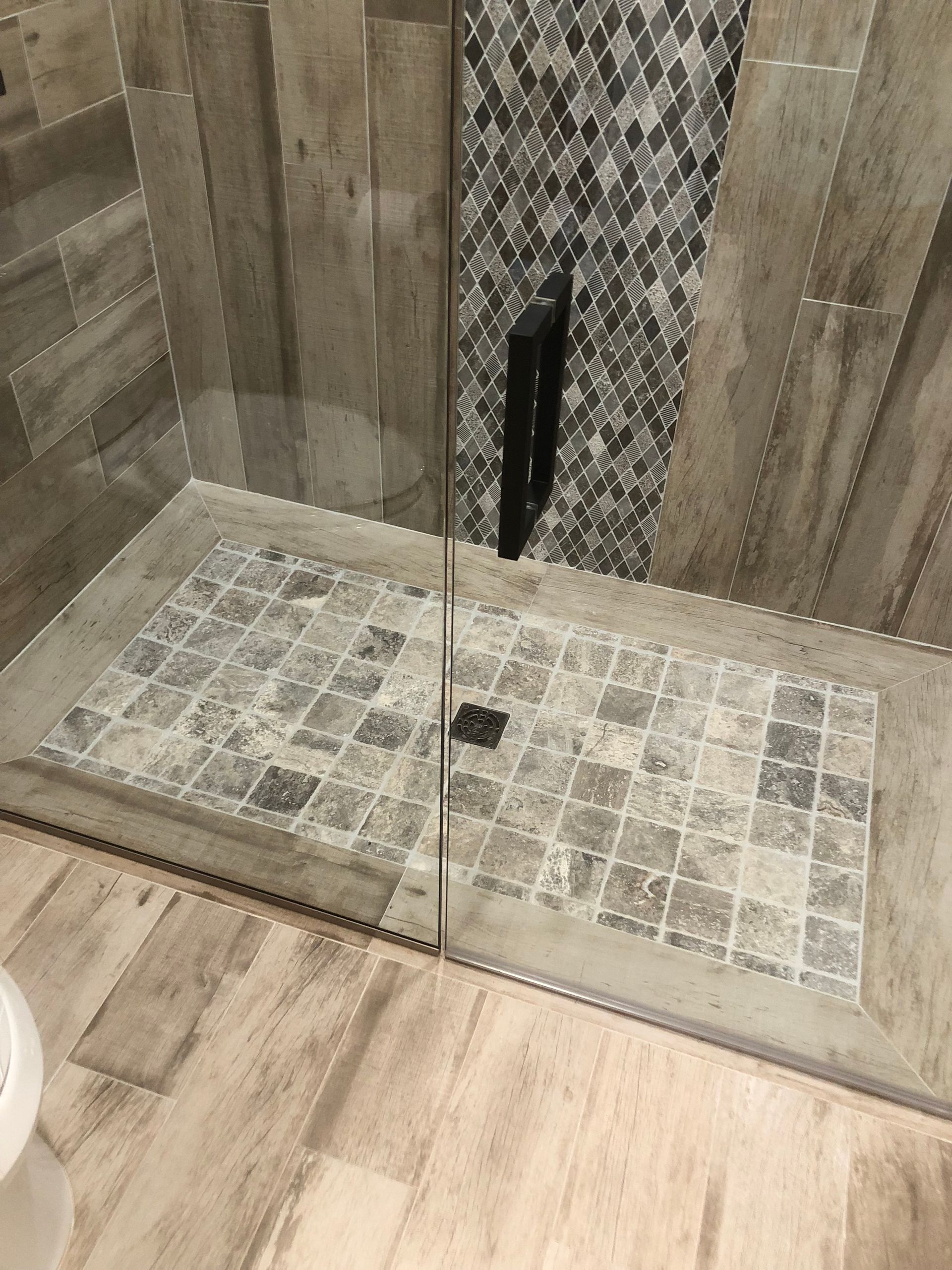 A walk in shower with a tiled floor and a glass door.