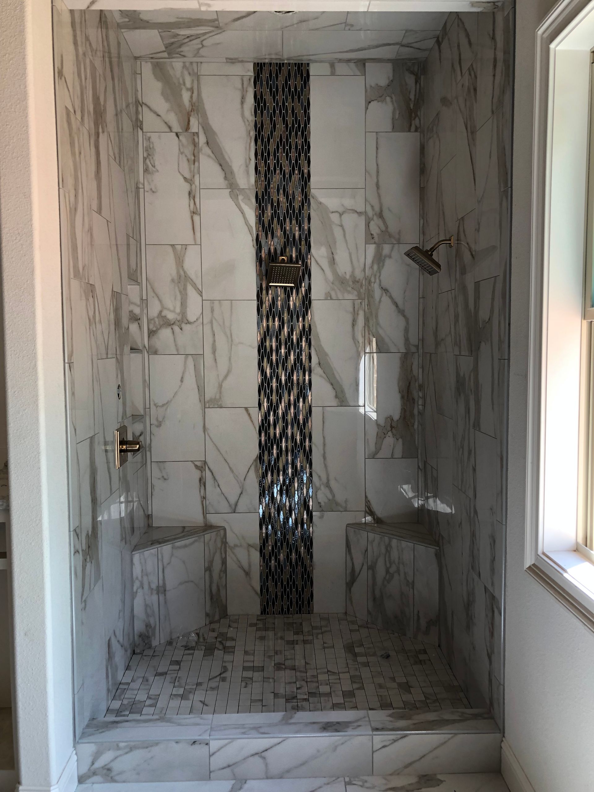 A bathroom with a walk in shower with marble tiles and a window.