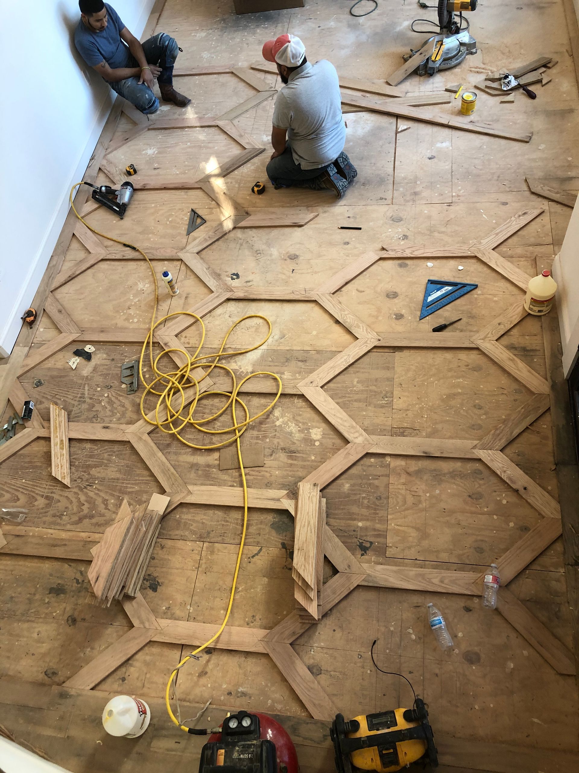 Two men are kneeling on a wooden floor in a room.