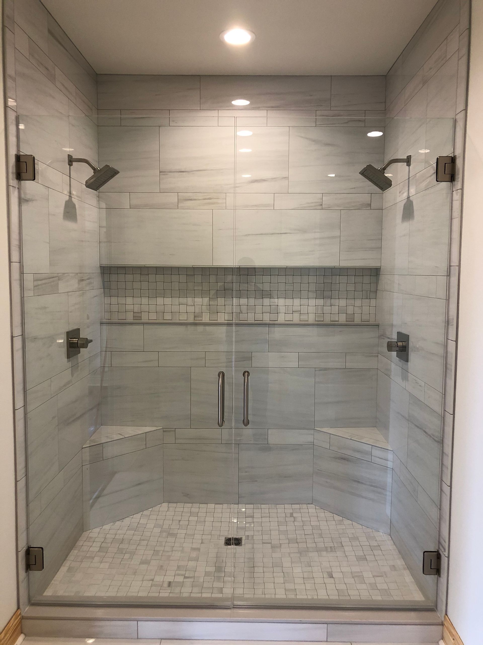 A shower stall with a glass door and two shower heads.