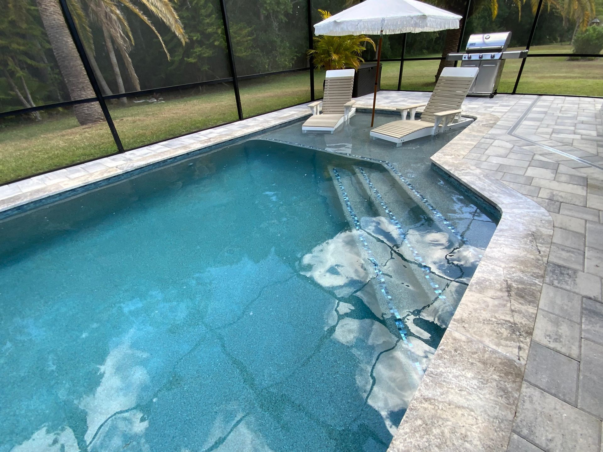 Person tiling a pool, using trowel to apply adhesive. Blue and white tiles, bucket of mortar.