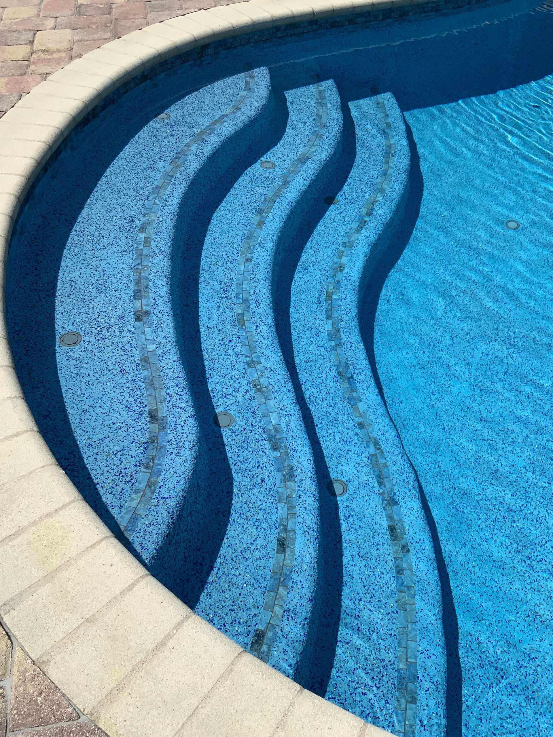 Blue tiled curved pool steps leading into clear water.