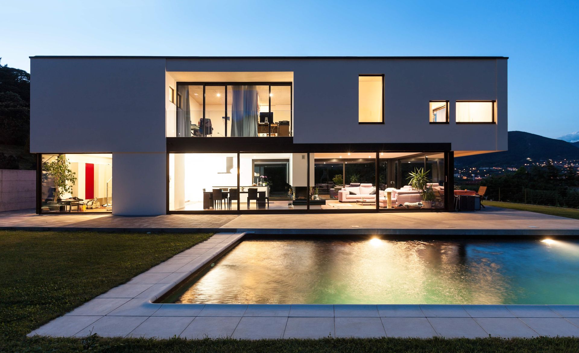 Modern home with glass walls, pool, and night lighting.