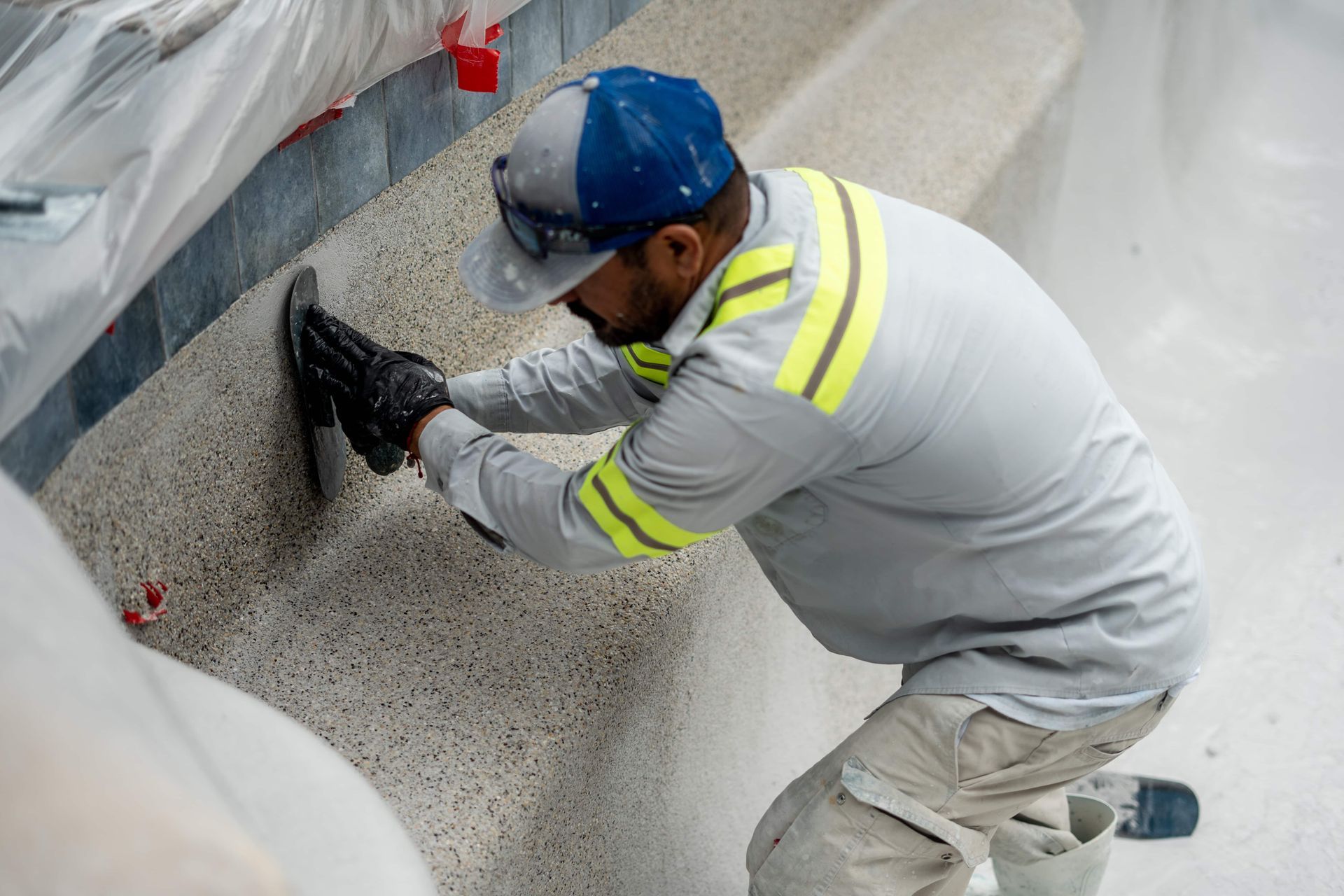 Man applying plaster to the interior wall of a swimming pool, wearing safety gear.