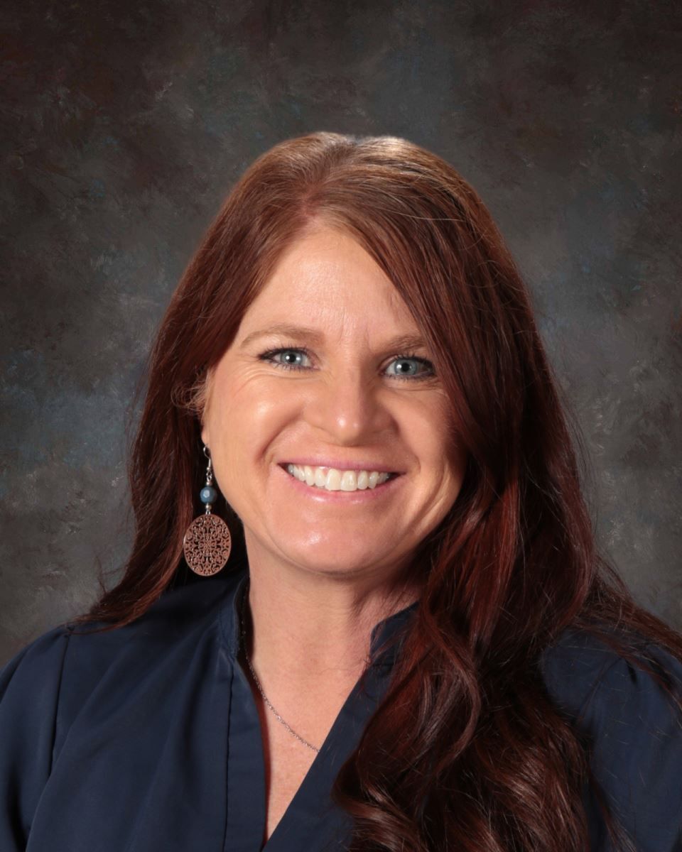 A woman wearing a blue shirt and earrings is smiling for the camera.