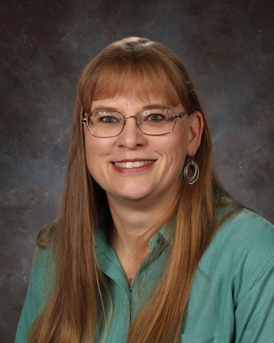 A woman wearing glasses and a floral shirt is smiling for the camera.